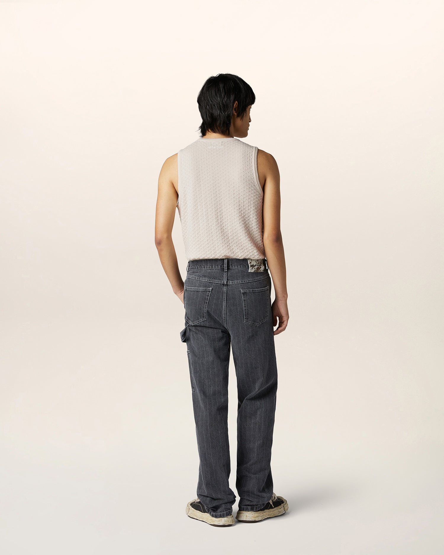 Back view of textured merino wool sleeveless vest tucked into relaxed pinstripe carpenter jeans — contemporary luxury menswear styling.
